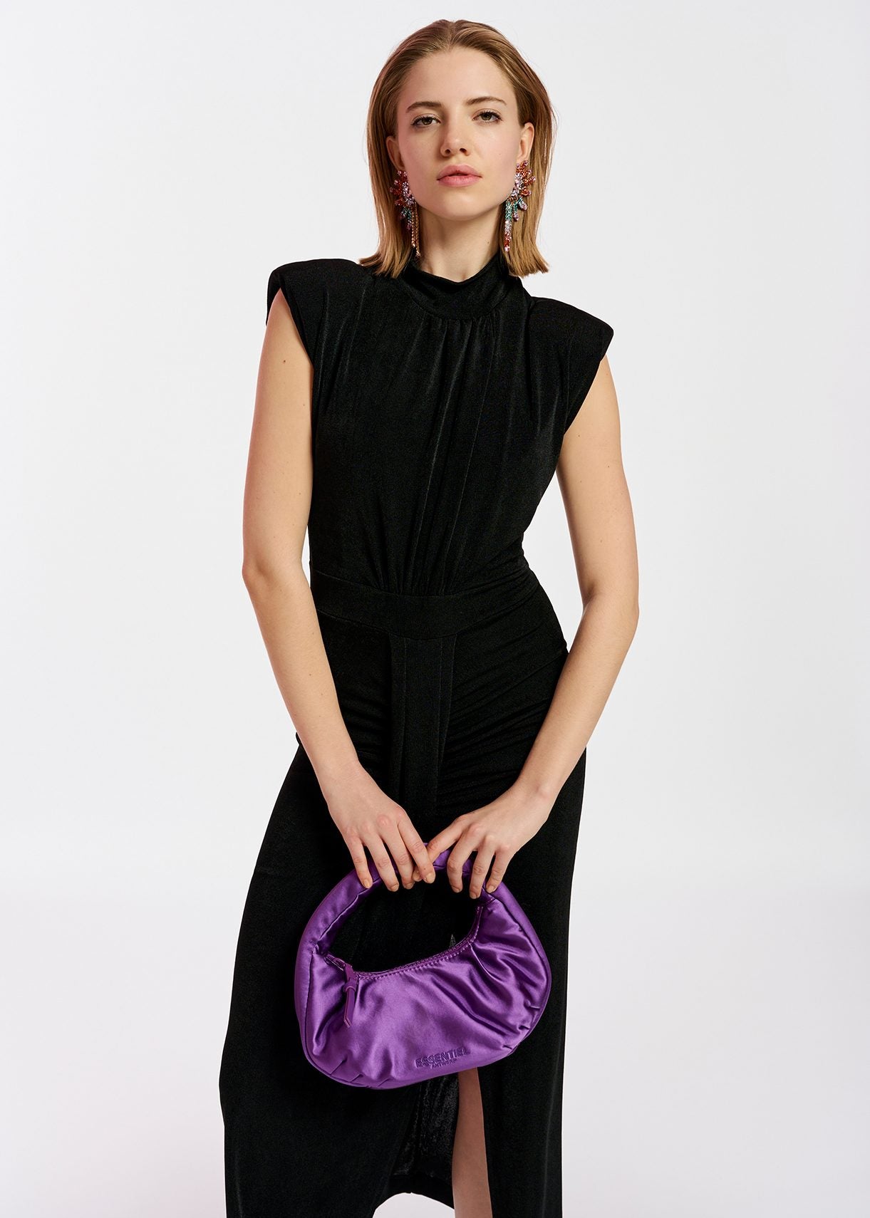 Model wears black midi dress with pleat and slit at front.