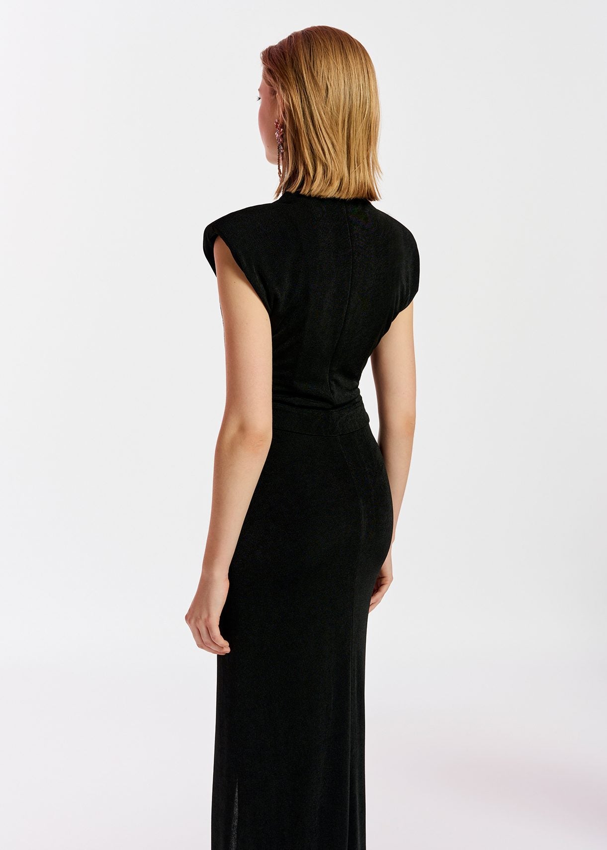 Model wears black midi dress with pleat and slit at front. Back view.