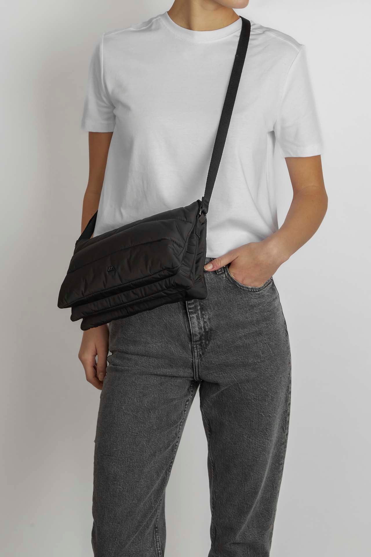 Person wearing a white t-shirt and gray jeans with a black Markberg Enea Crossbody Bag made from recycled plastic bottles.