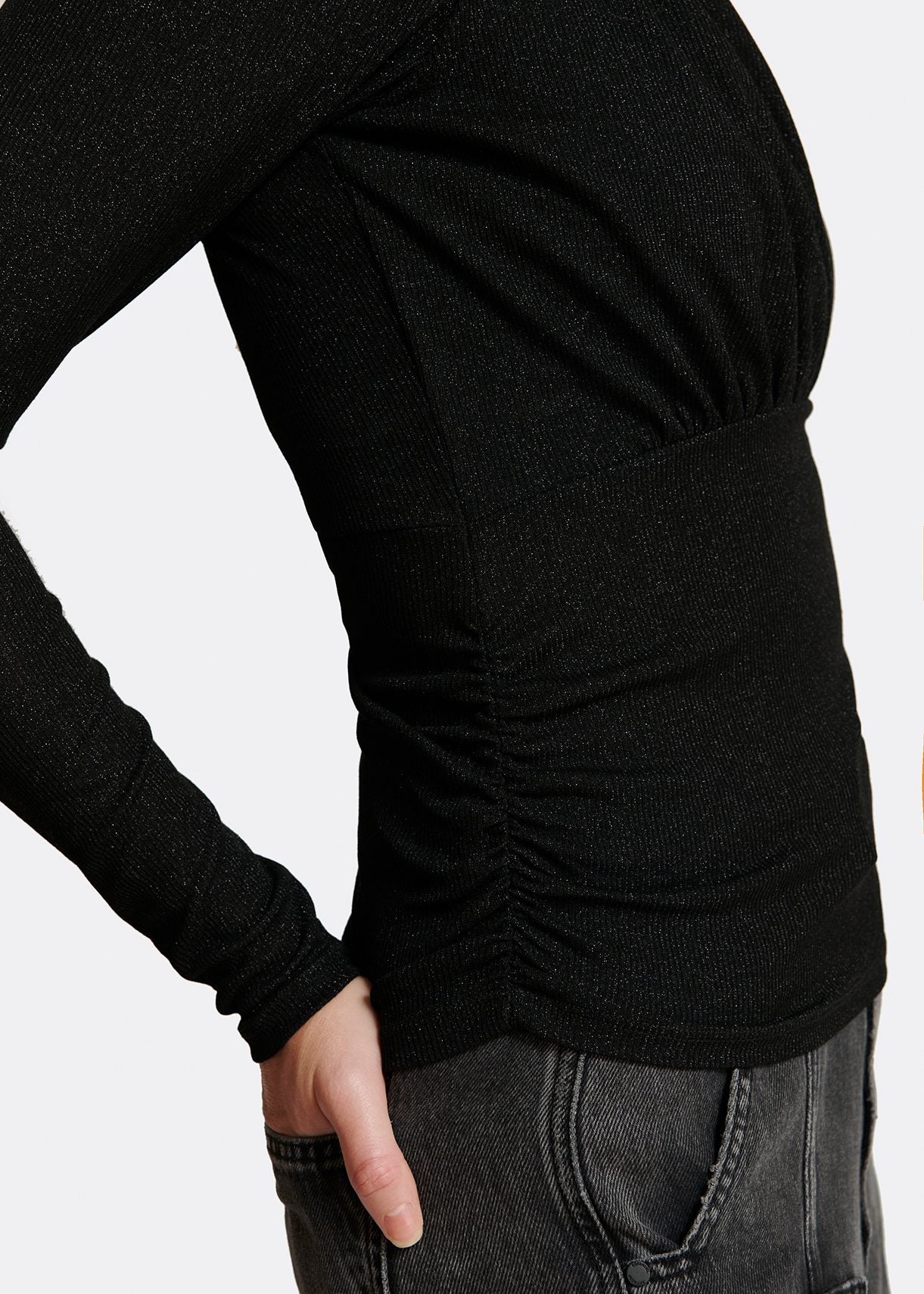 Model wears black long sleeve top with ruching on chest. Side view.
