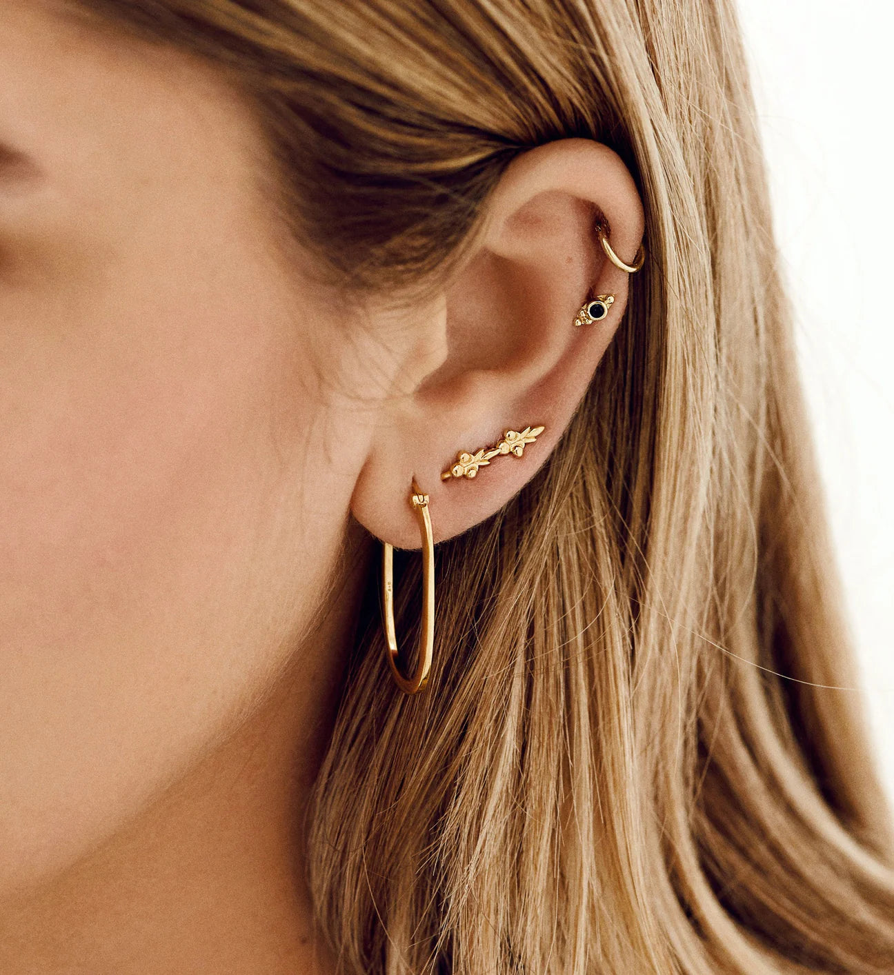 A woman wearing a pair of Anna + Nina Link Hoop Earring - Goldplated with a geometric shape.