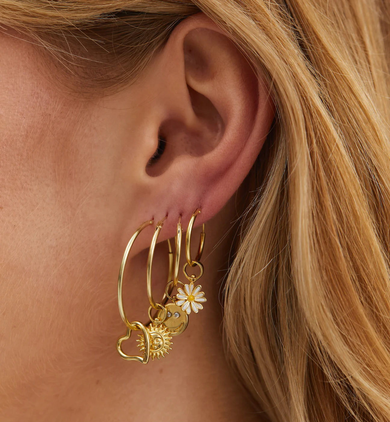 A woman's ear with Anna + Nina gold plated hoop earrings and a Heart Charm - Gold.