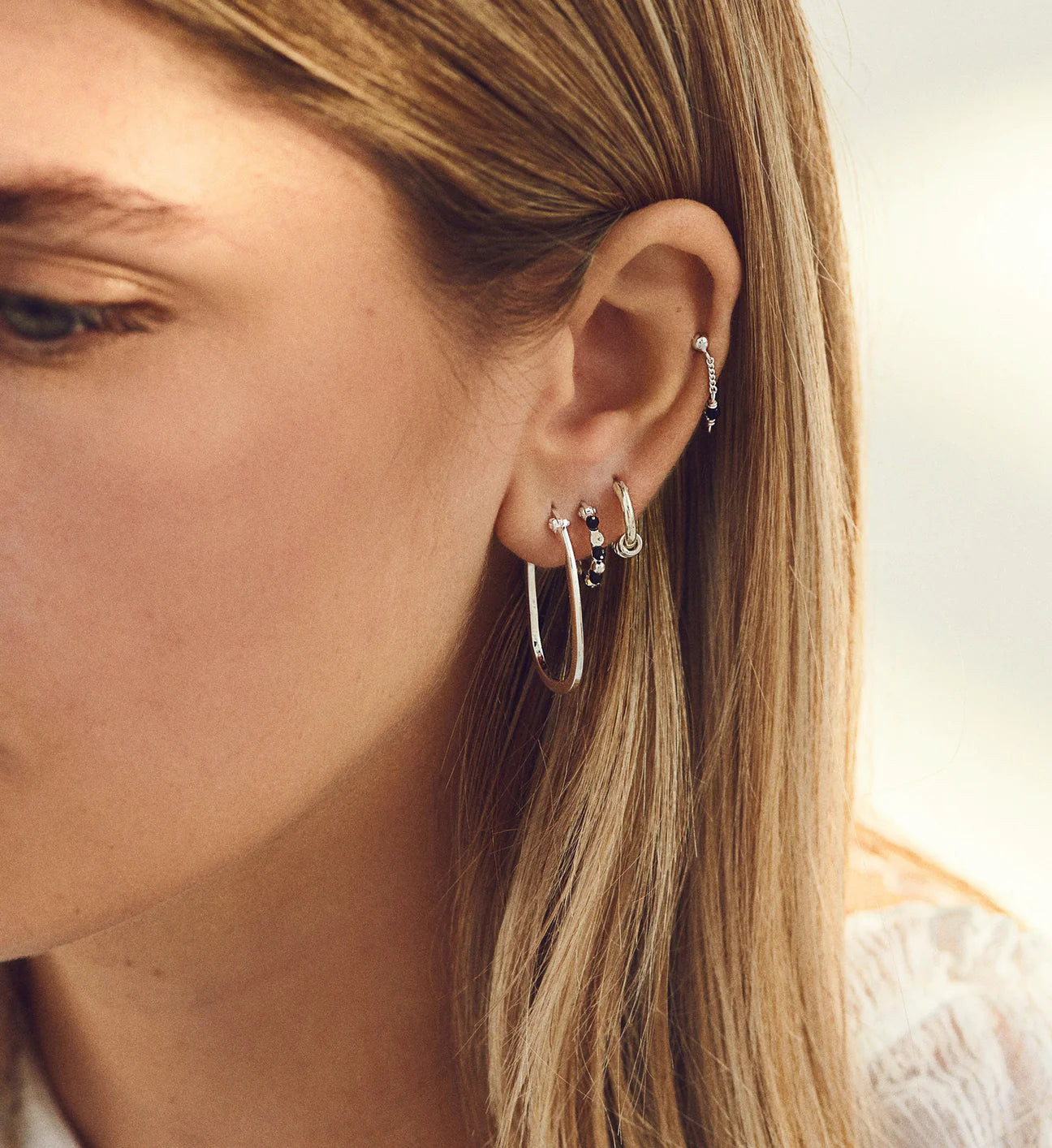 A woman wearing a pair of Anna + Nina's Link Hoop Earring - Silver, made from silver materials.