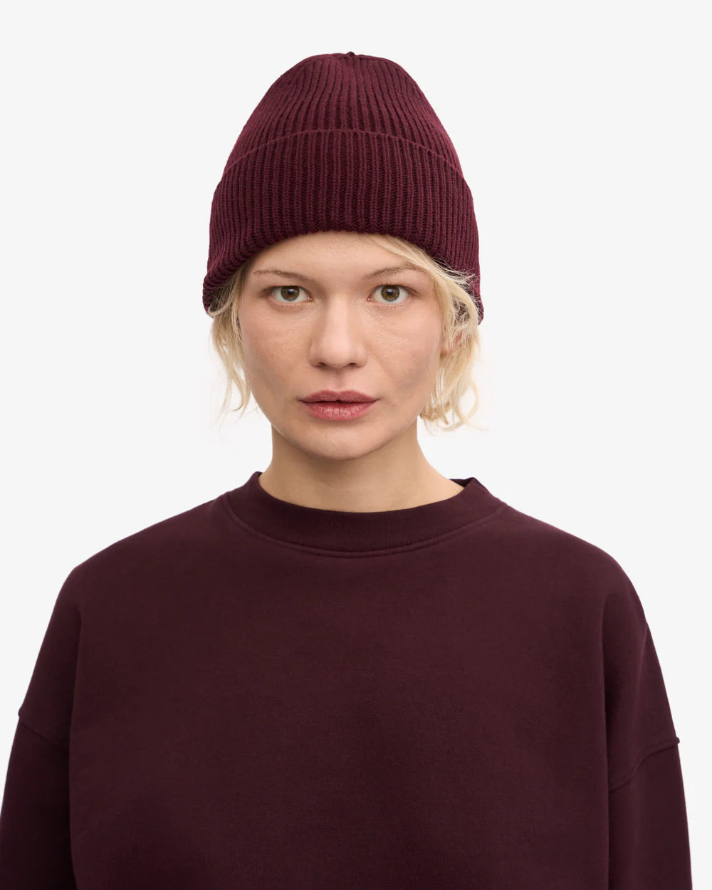 A person wearing a burgundy Colorful Standard Merino Wool Beanie and matching sweatshirt stands against a plain white background, facing the camera.