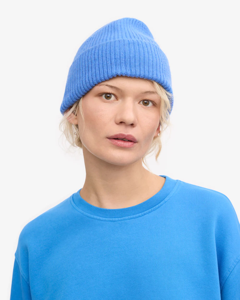 Against a plain white background, a person wears the Colorful Standard Merino Wool Beanie in light blue with a matching sweatshirt.