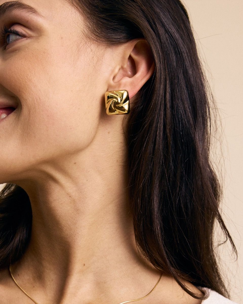 Close-up of a woman's ear adorned with EDBLAD's Milky Way Studs S in 14K gold plating, showing part of her smiling face and neck.