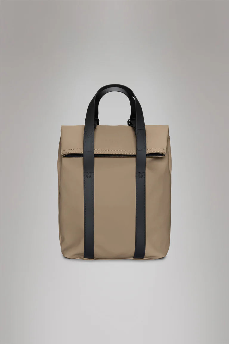 The Rains 2 Way Tote Backpack Mini is a beige rectangular commuter bag with a top flap, black vertical straps, and two black handles, ideal for on-the-go use. Shown against a plain gray background.