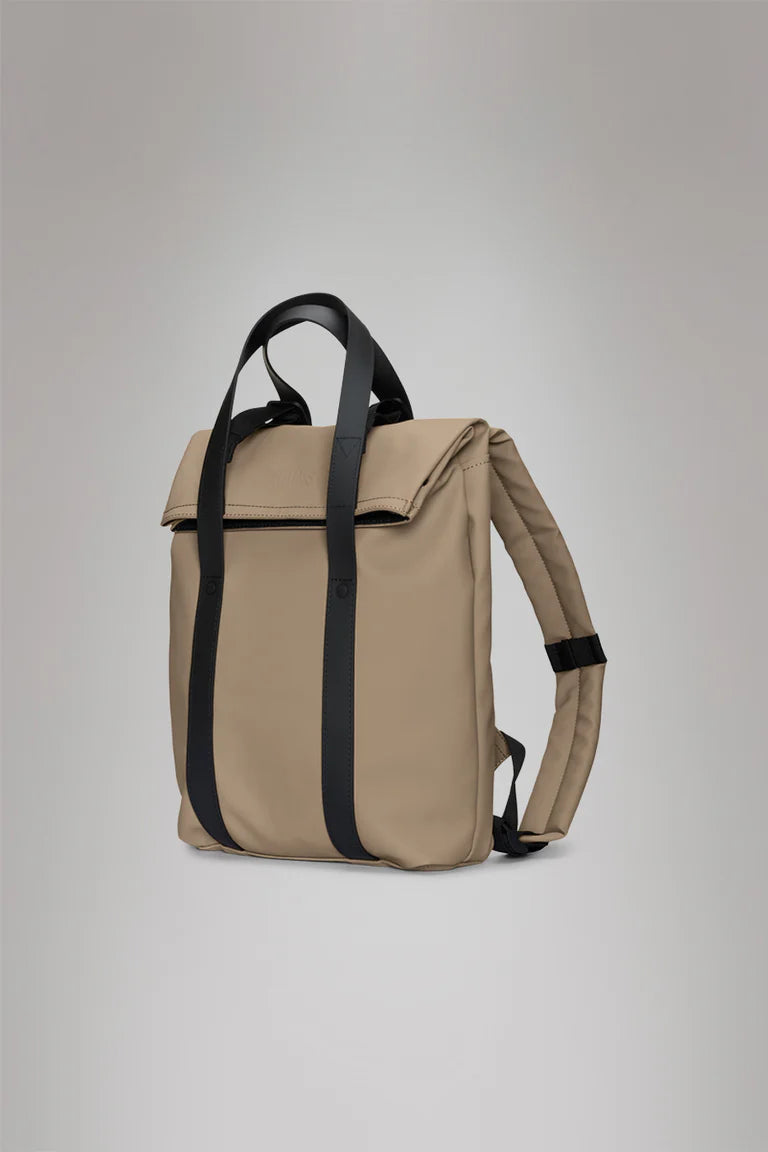 The Rains 2 Way Tote Backpack Mini is a beige, rectangular bag with black straps and a fold-over top, perfect for commuters and style-conscious users, shown against a plain light gray background.