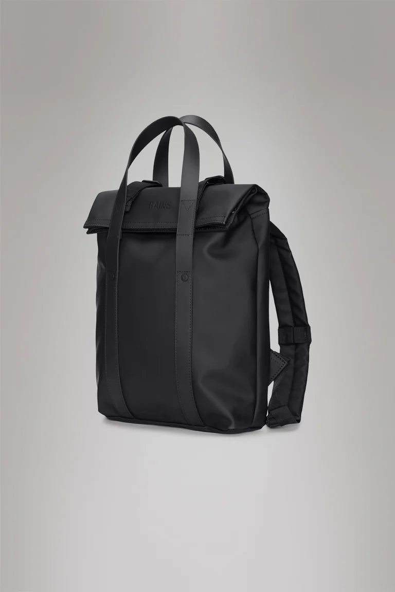 The Rains 2 Way Tote Backpack Mini, a black rectangular bag with dual top handles, front flap, and adjustable straps, offers commuter-friendly style—shown here against a plain grey background.