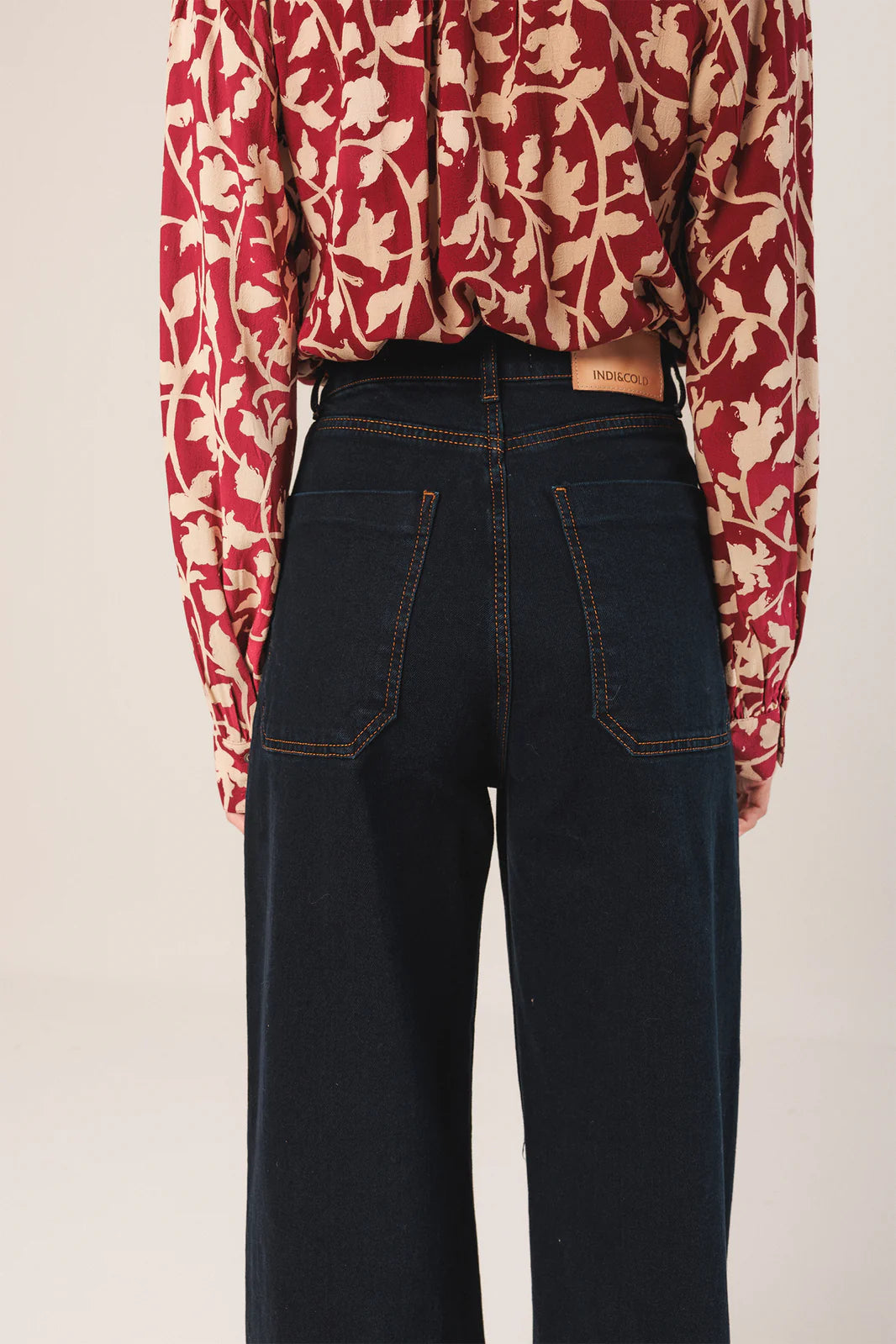A person wears a red and beige floral shirt tucked into Indi & Cold Wide Leg Denim Trousers - Navy, featuring patch pockets, photographed from the back.