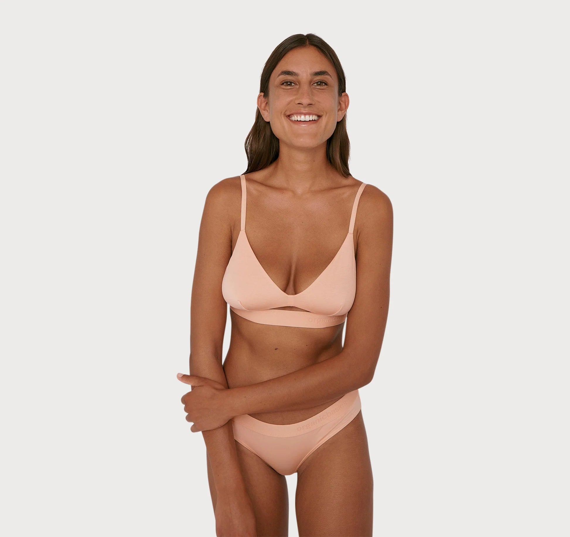 A woman in a peach bikini top and bottom made of sustainable TENCEL, the Soft Touch Tanga 2-Pack in Soft Pink by Organic Basics, the softest fabric for the comfiest fit.