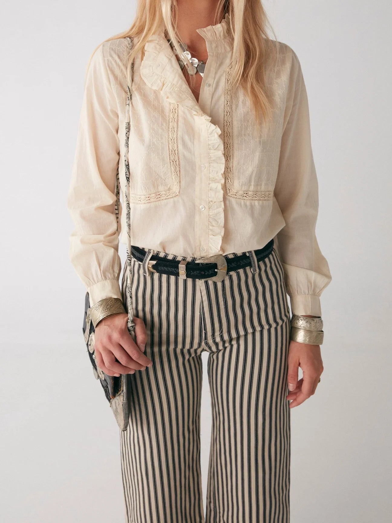 A woman wearing the Maison Hotel Riya Blouse - Victorian Ivory with embroidery, paired with striped pants.