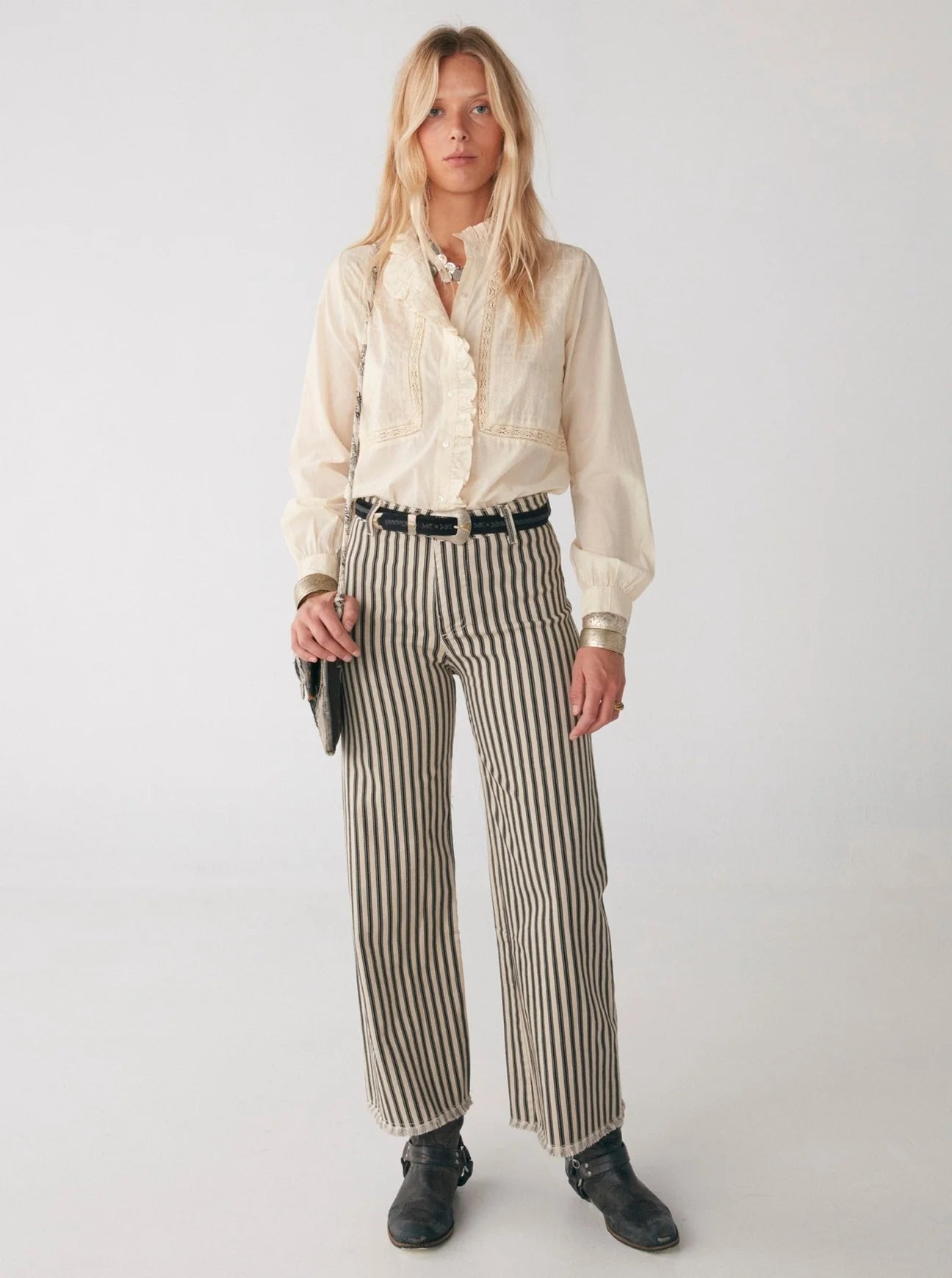 A woman wearing striped pants and a Riya Blouse - Victorian Ivory with embroidery from Maison Hotel.