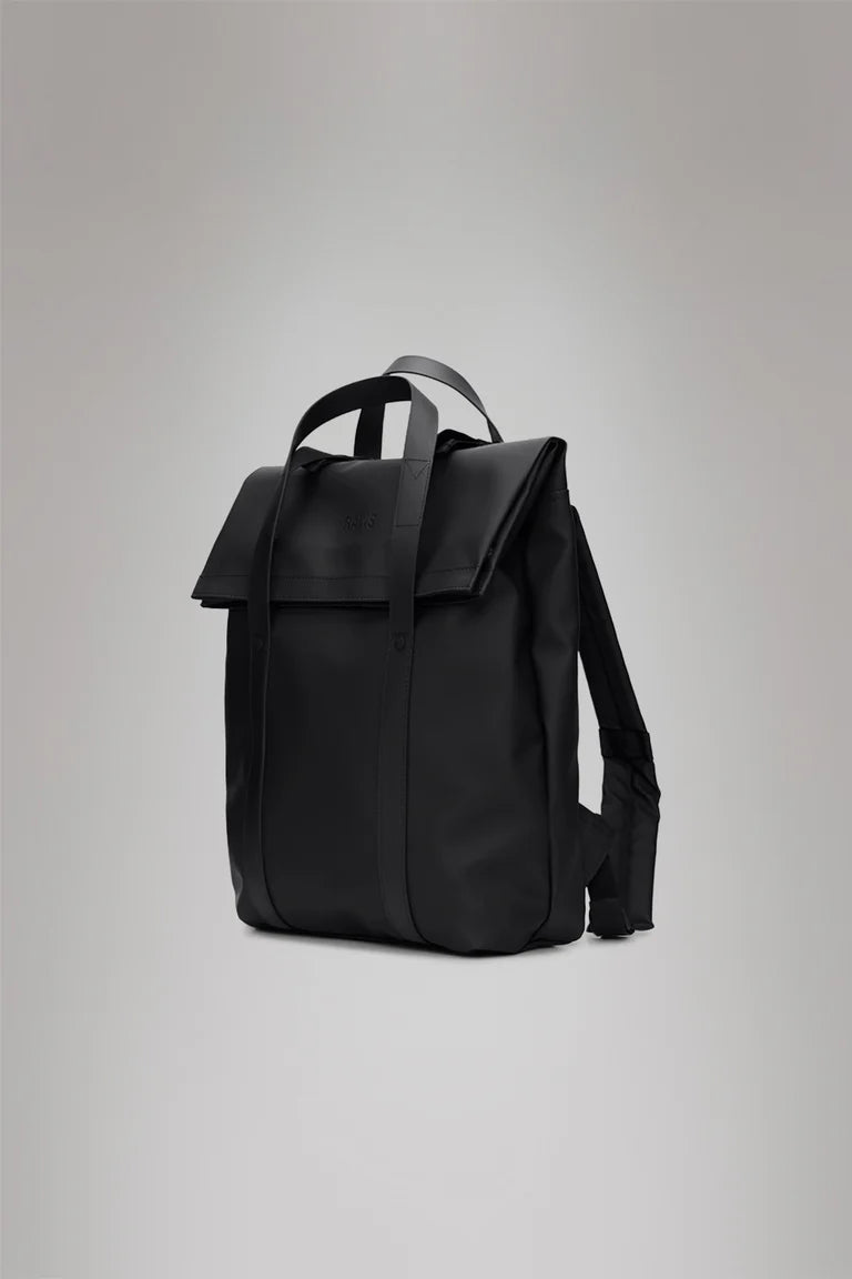 The Rains 2 Way Tote Backpack in black features a flap closure, two top handles, and adjustable shoulder straps, shown against a plain gray background.