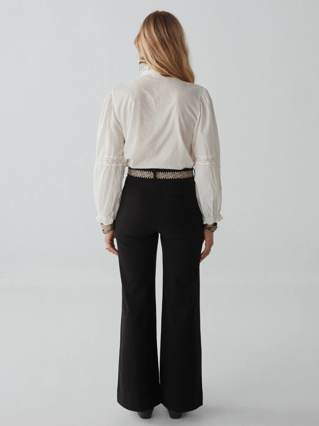 woman with blond hair wears a white embroidered blouse and long black jeans and boots maison hotel