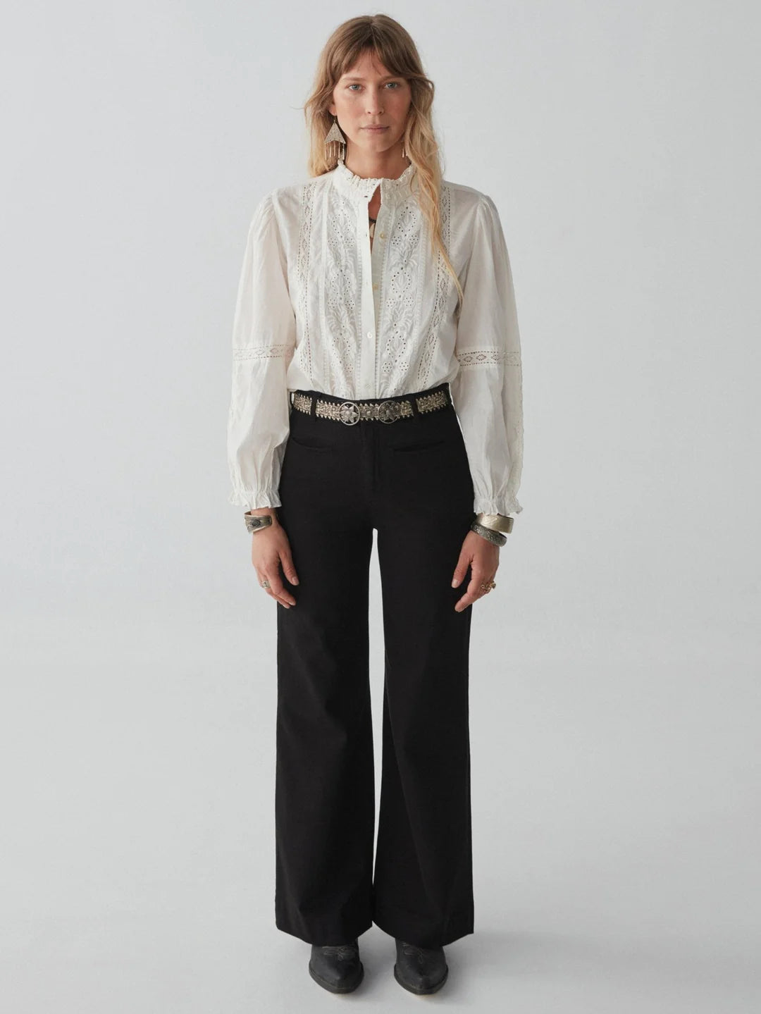 woman with blond hair wears a white embroidered blouse and long black jeans and boots maison hotel