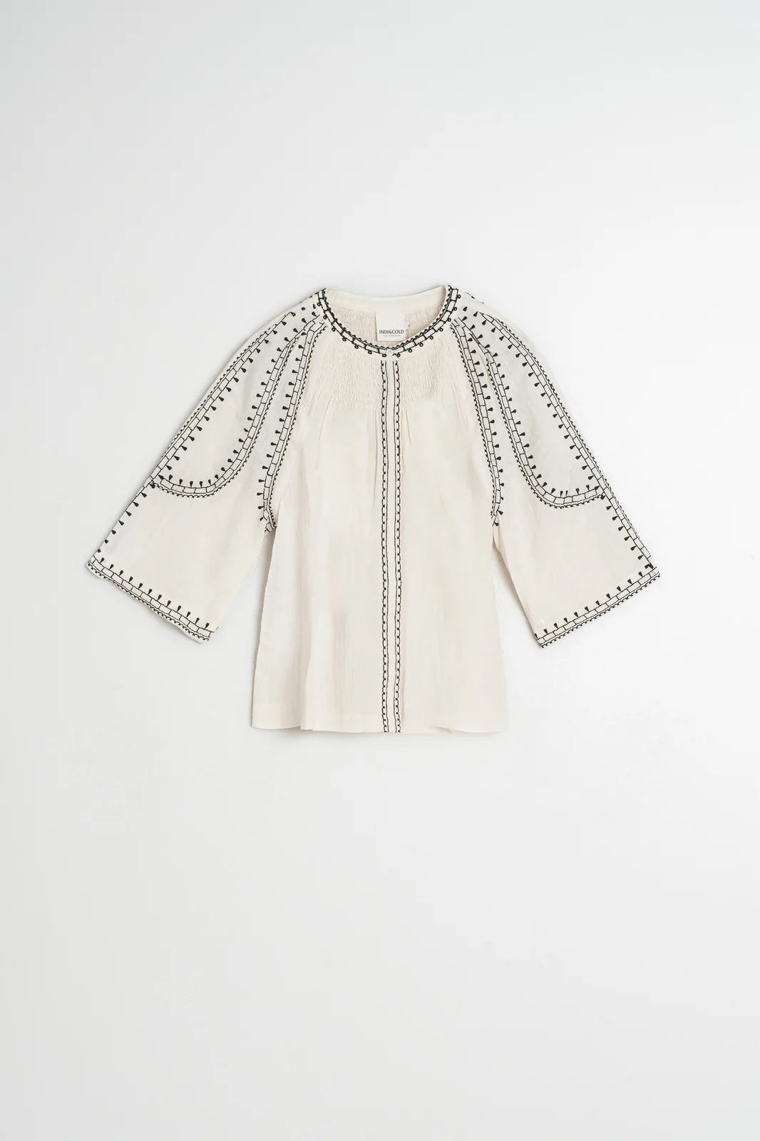 The Indi & Cold Embroidered Blouse - Off White is crafted from organic cotton and features black embroidery along the seams and edges, shown against a plain white background.