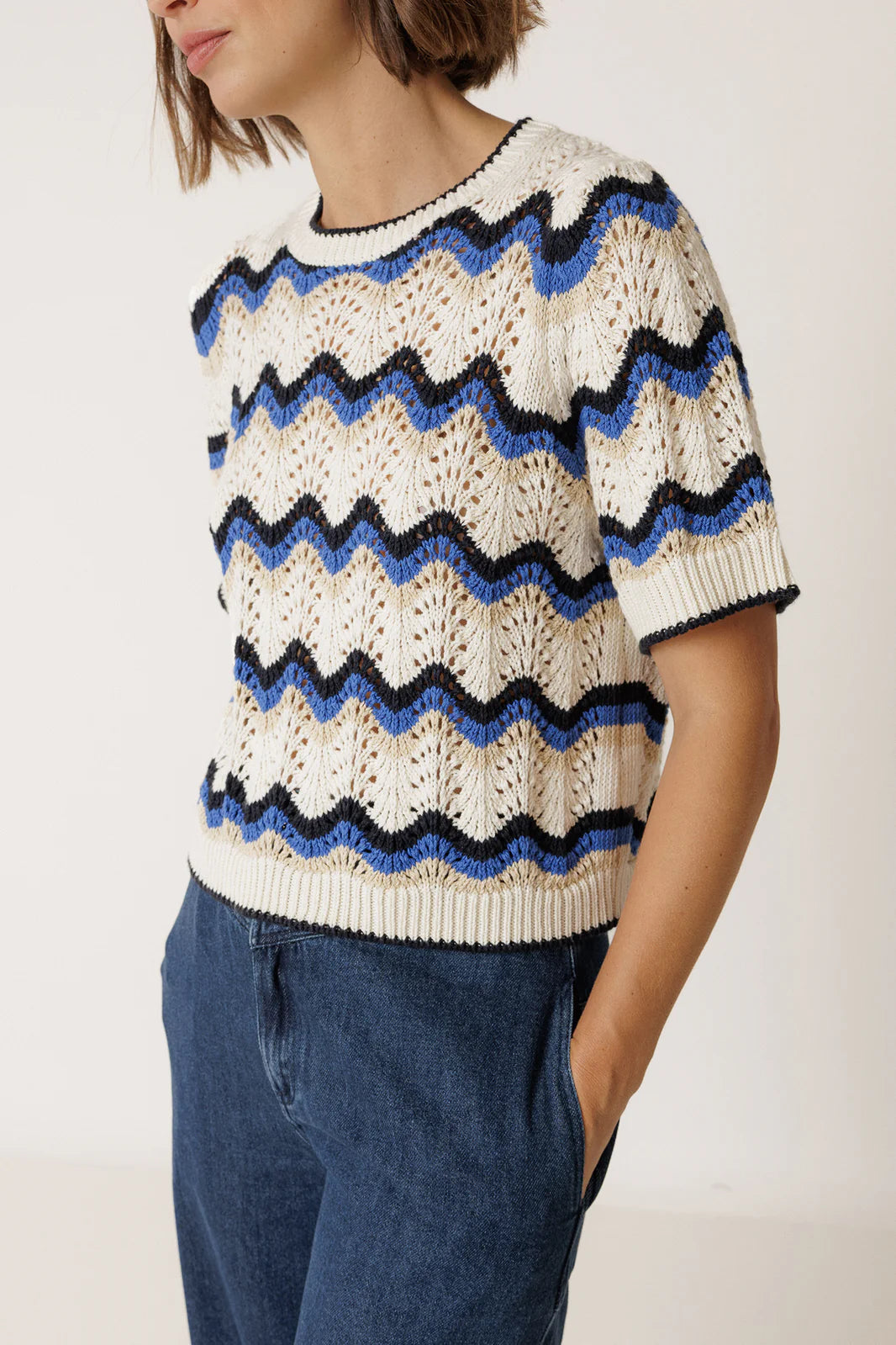 A person wearing the Indi & Cold Wavy Crochet Sweater - Blue with high-waisted blue jeans, standing with hands in pockets.
