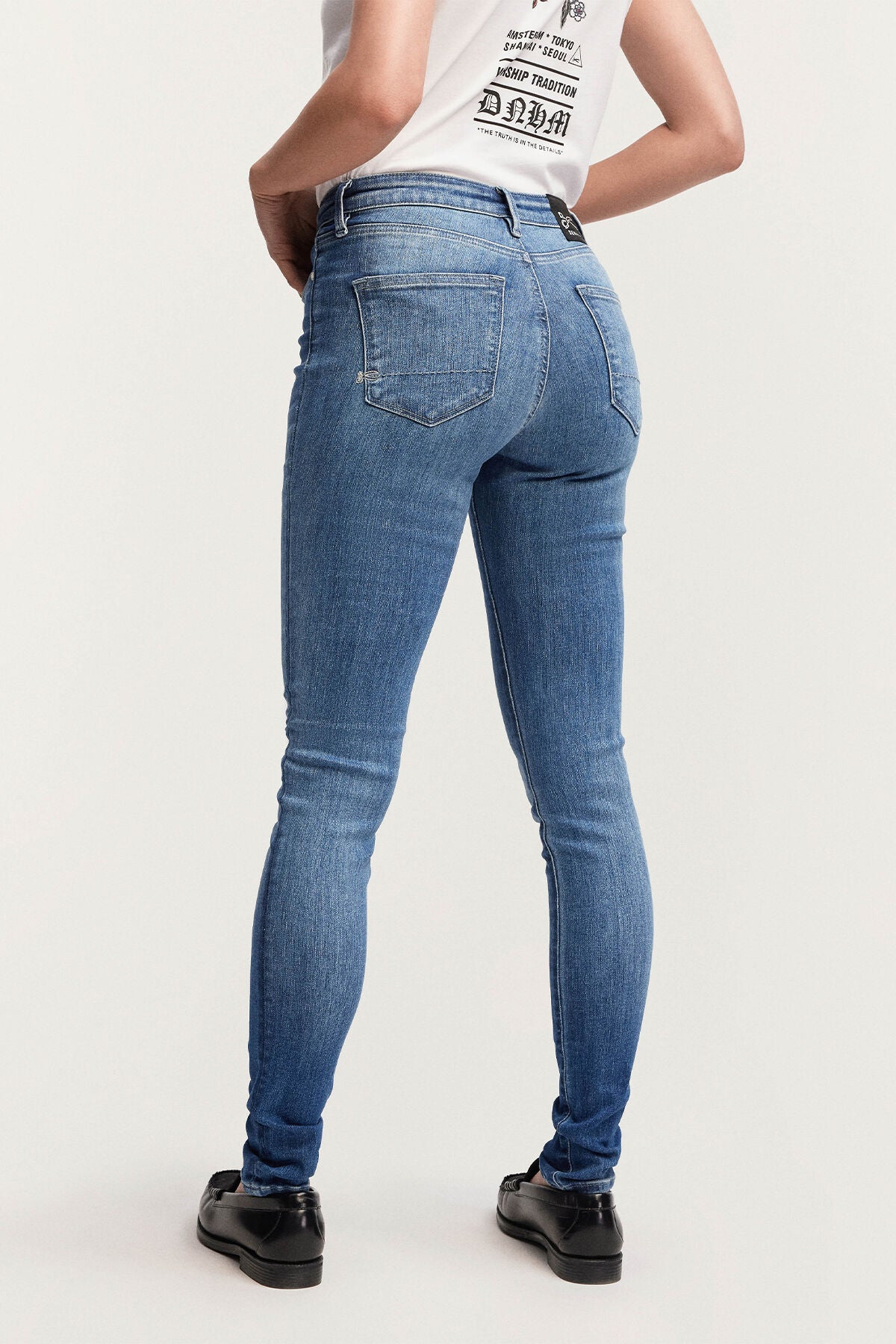 The back view of a woman wearing Denham high-rise skinny denim jeans in NEEDLE Skinny - Light Indigo and a white t-shirt.