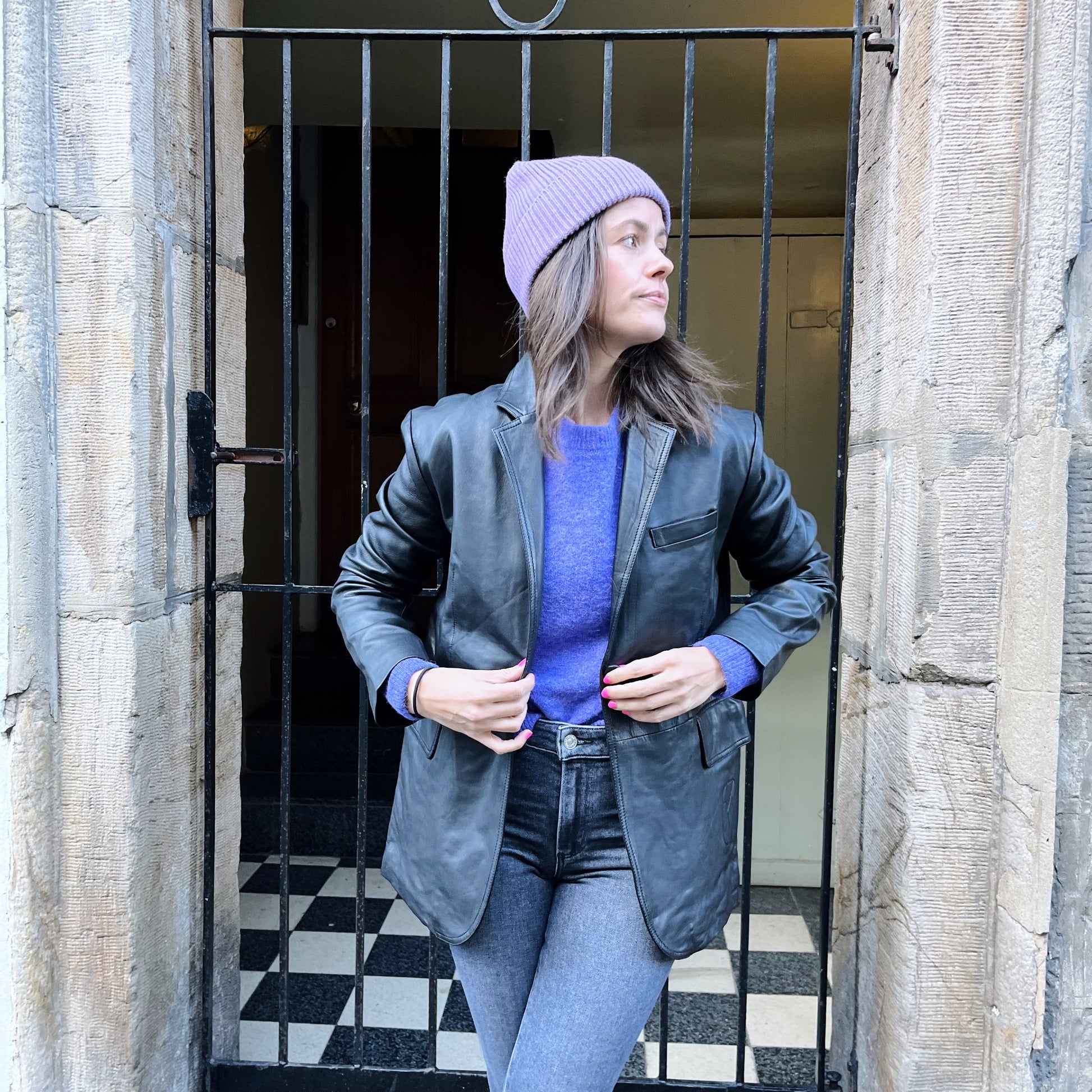 A woman sporting a MDK Celaya Classic Blazer - Black, fashioned in lambskin leather and topped with a stylish purple beanie.