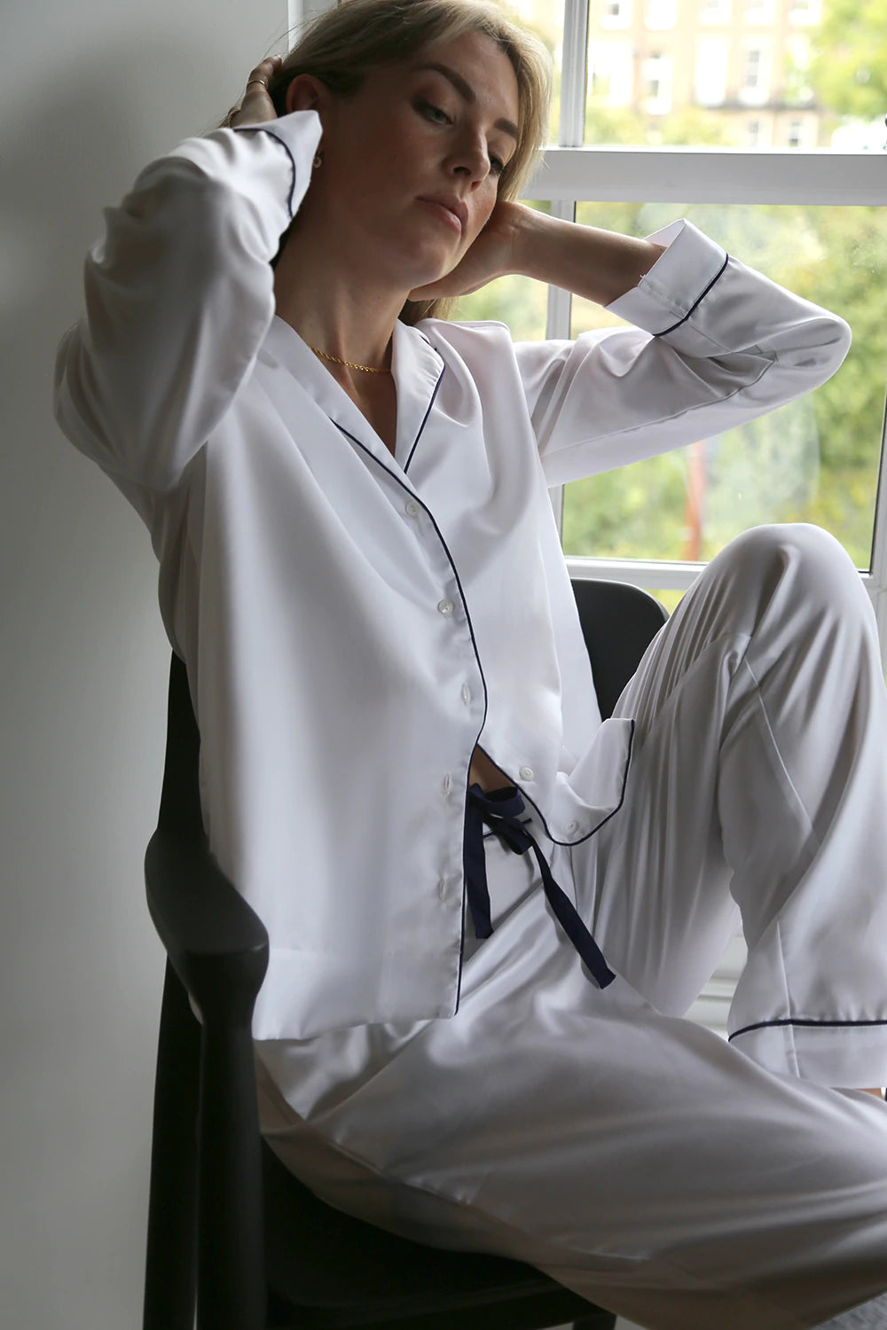 A woman in a BREATHE Organic Cotton Pyjama Set - Herringbone White, made from organic cotton, sitting on a chair.