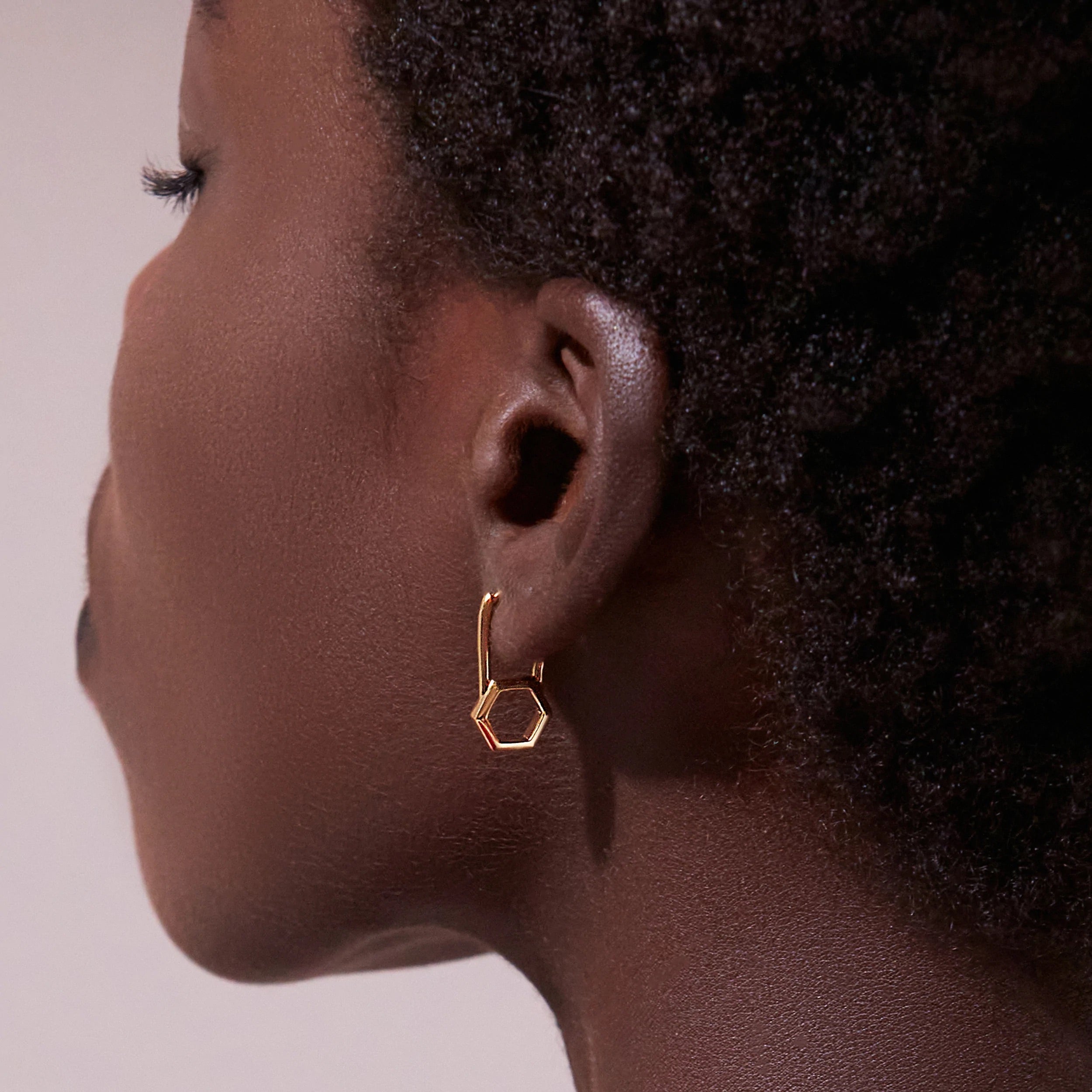 A woman's ear with a Rachel Jackson London Hex Padlock Hoop earring, showcasing elegant jewellery.