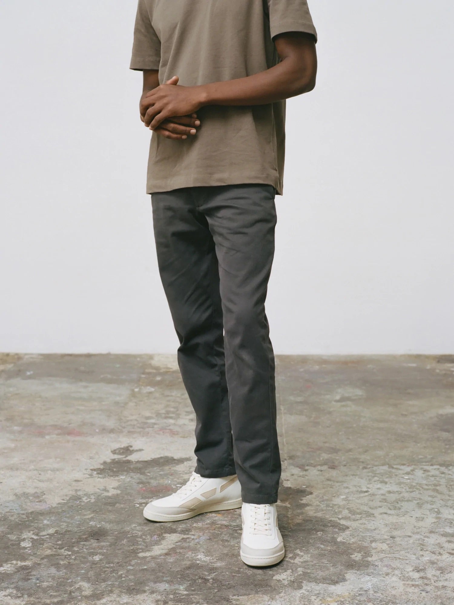 A man wearing a grey t-shirt and gray pants walks confidently, his SAYE Modelo '89 Hi Sneakers - Beige effortlessly blending comfort and style.