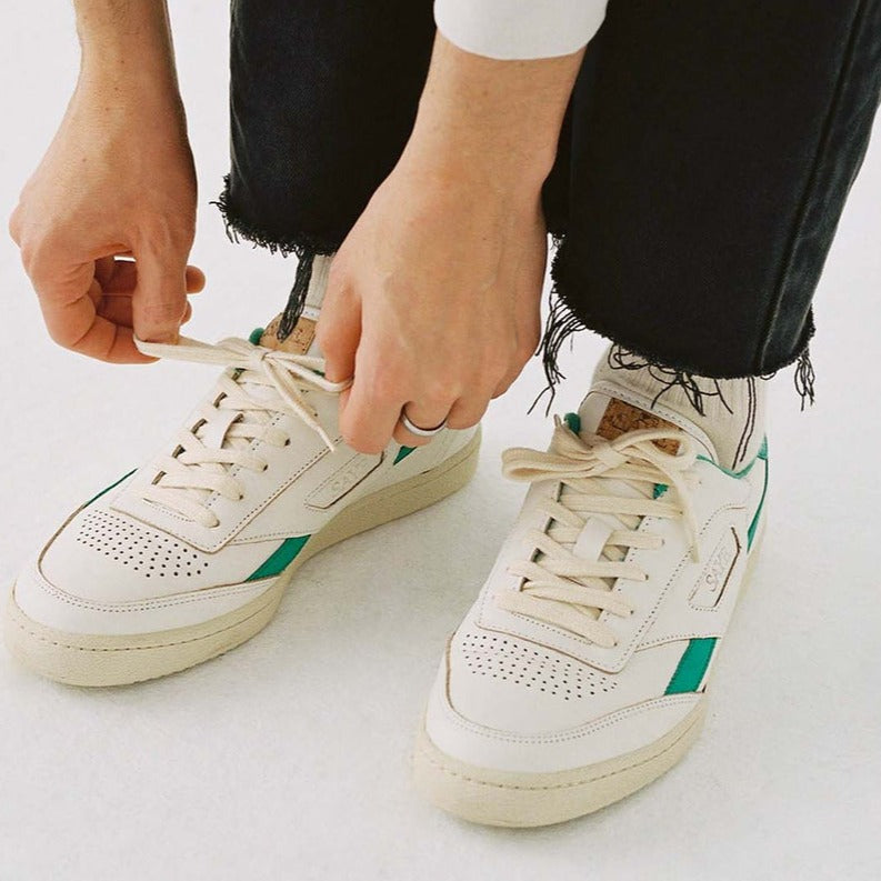 A person is tying up a pair of SAYE Modelo '89 Sneakers - Green made from vegan Napa.