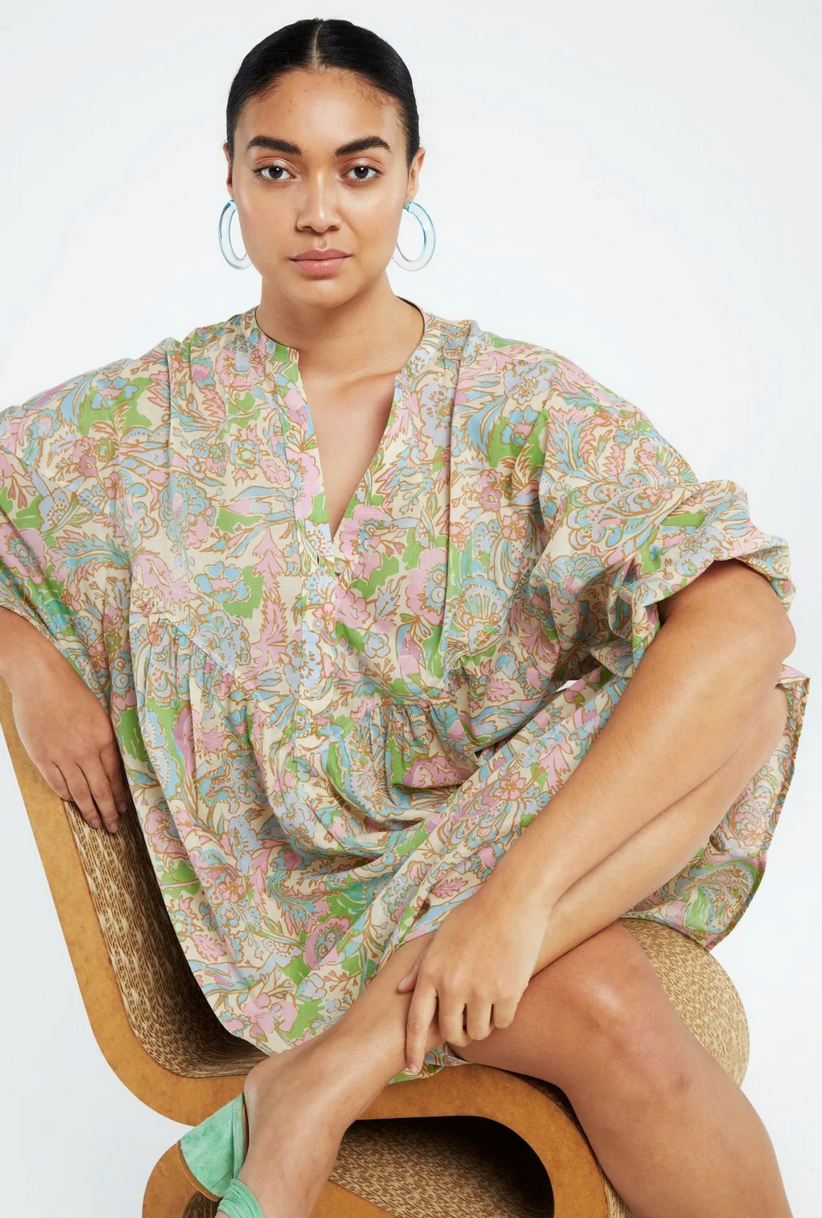 The model is sitting on a chair in a paisley Dover Dress - Acapulco Pink made of organic cotton by Fabienne Chapot.