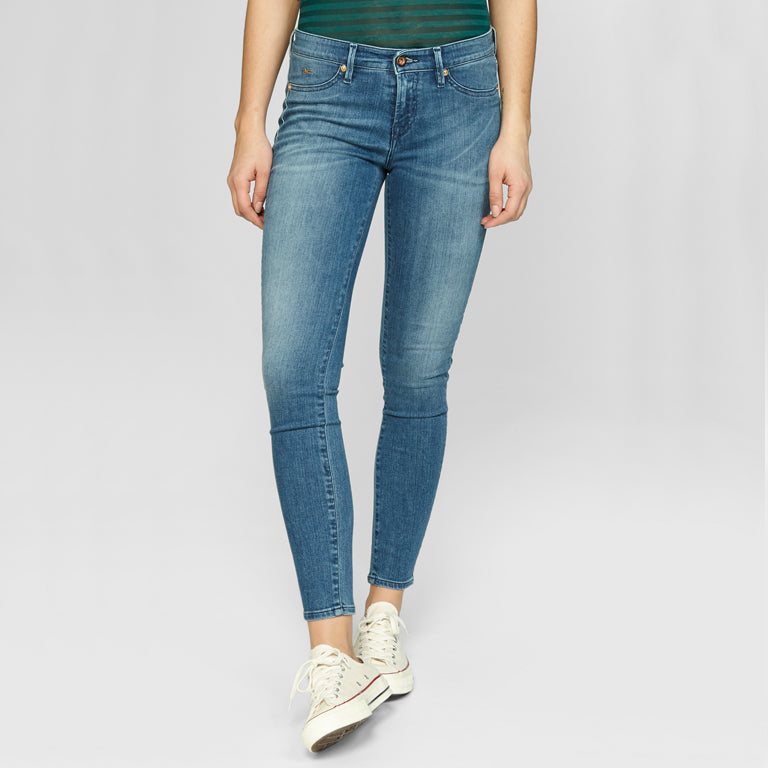 A woman wearing Denham's SPRAY Skinny - Golden Rivet Prosecco blue jeans and a green t-shirt.