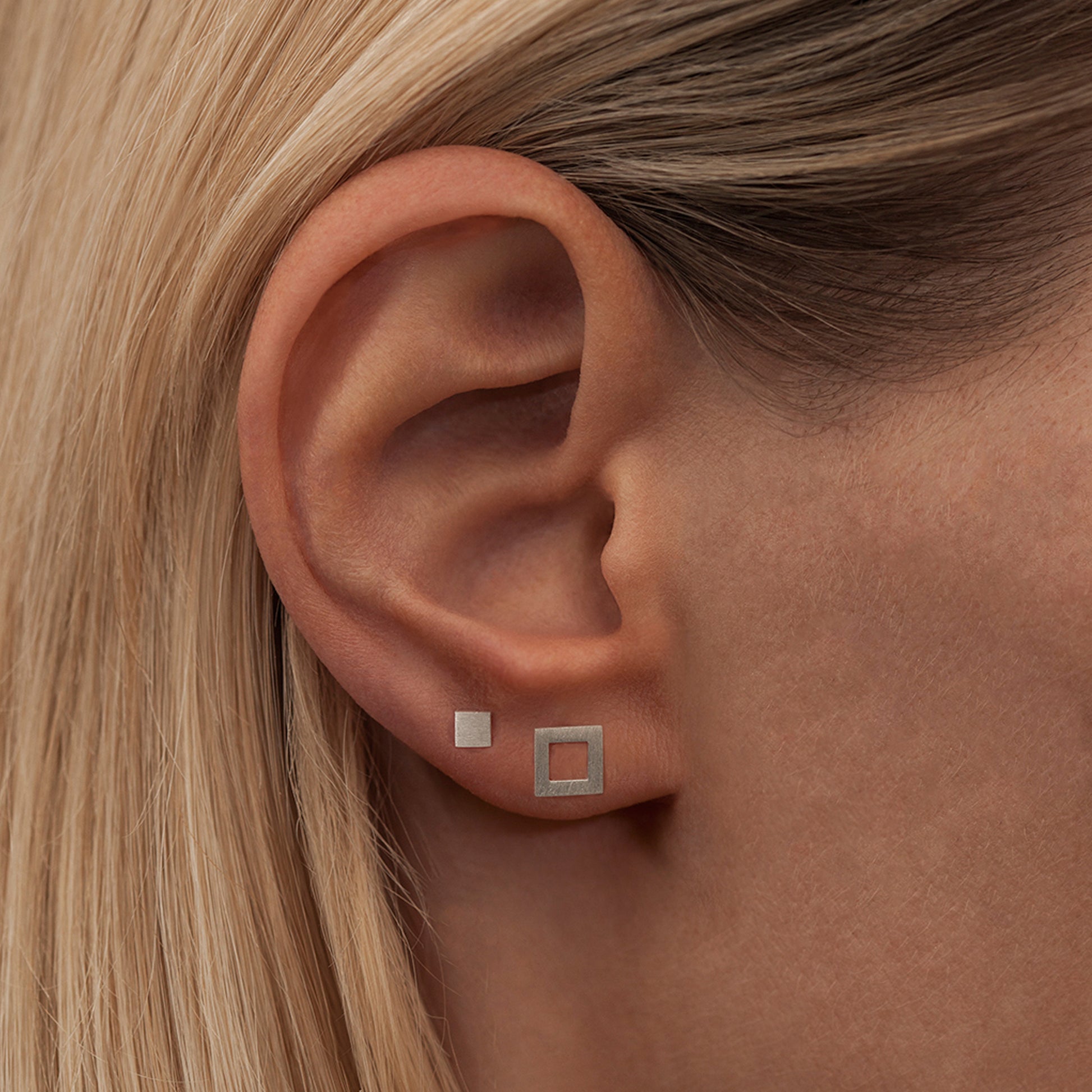 A woman's ear adorned with a Lulu Copenhagen silver square stud earring, featuring a brushed silver finish.