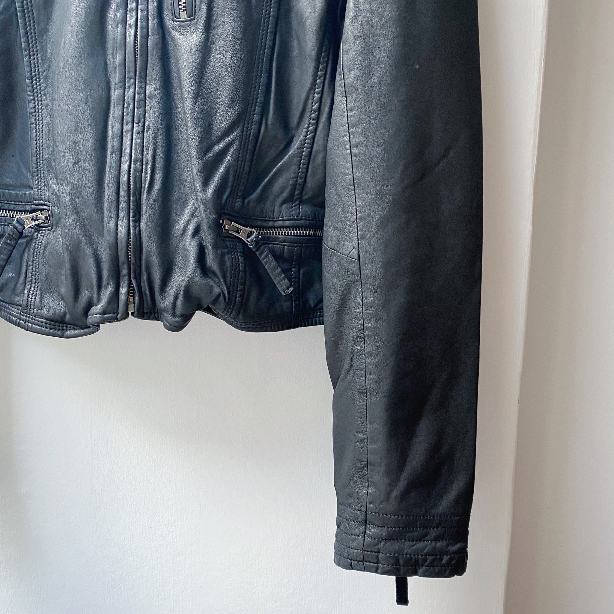 A fitted MDK black Leather Rucy Jacket hanging on a wall.