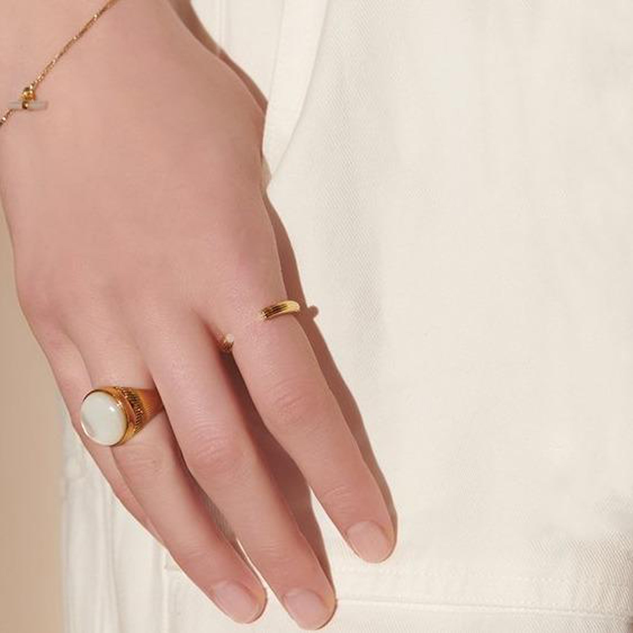 A woman's hand with a gold ring featuring an Art-Deco detailing and a white stone open Ridged Mother of Pearl ring - Gold with Rachel Jackson London stones.