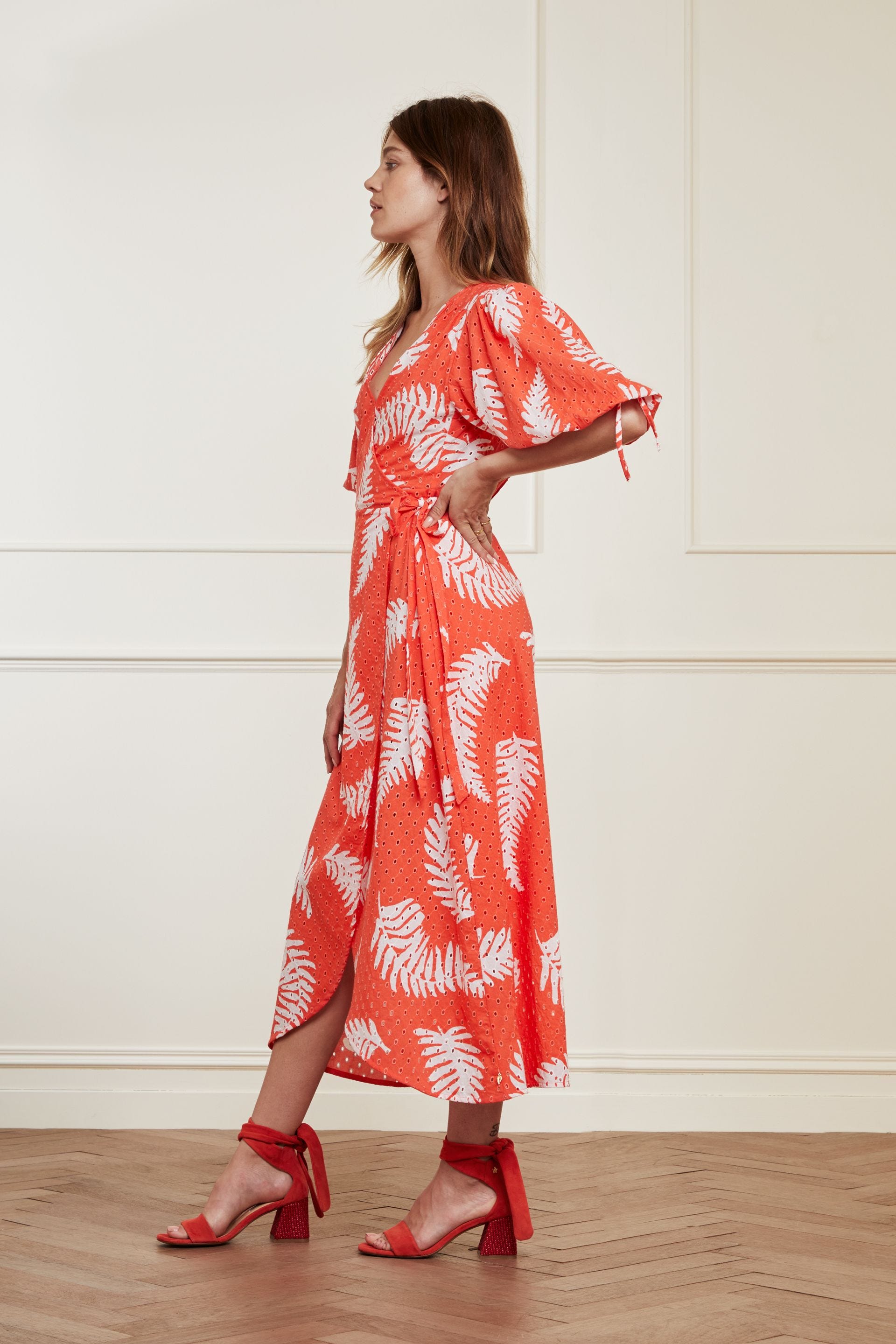 A feminine woman wearing a Charlie Broderie Dress - Hot Coral by Fabienne Chapot, made of 100% GOTS-certified cotton, featuring a v-neckline.
